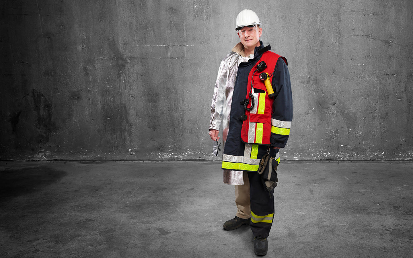Fotomontage eines Mannes: Halb Stahlingenieur in silberner Hitzeschutz-Arbeitskleidung, halb Feuerwehrmann in Uniform.