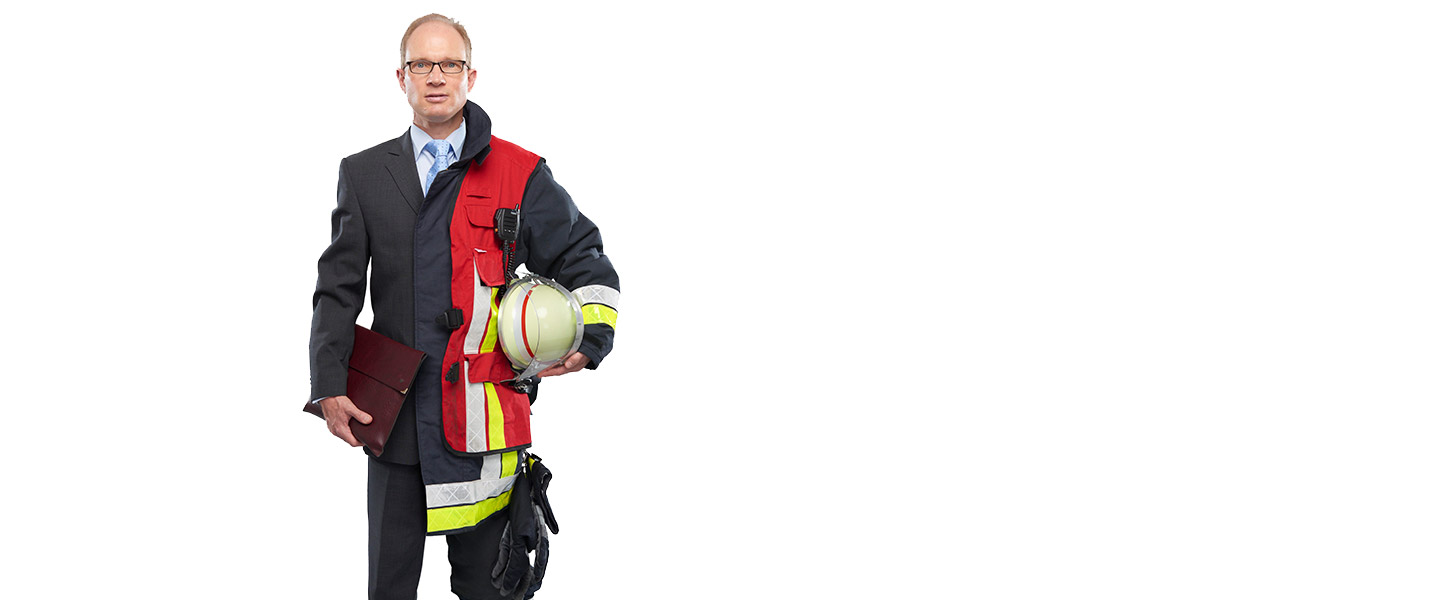 Fotomontage eines Mannes: Zur einen Hälfte im Businessanzug, zur anderen Feuerwehrmann in Uniform. Er hält eine Ledermappe und einen Feuerwehrhelm in den Händen.