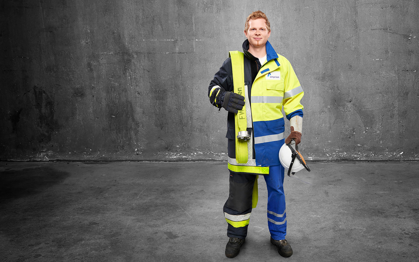 Fotomontage eines Mannes: Halb Hochspannungselektroniker in gelb-blauer Arbeitskleidung, halb Feuerwehrmann in Uniform. Er trägt einen Feuerwehrschlauch über der Schulter.