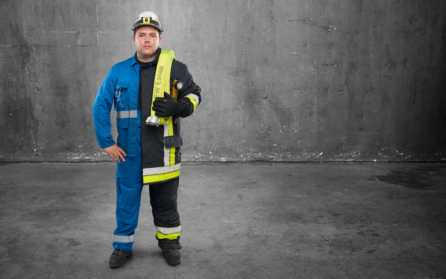 Fotomontage eines Mannes: Halb Kraftwerker in hellblauer Arbeitskleidung, halb Feuerwehrmann in Uniform. Er trägt einen Feuerwehrschlauch über der Schulter.