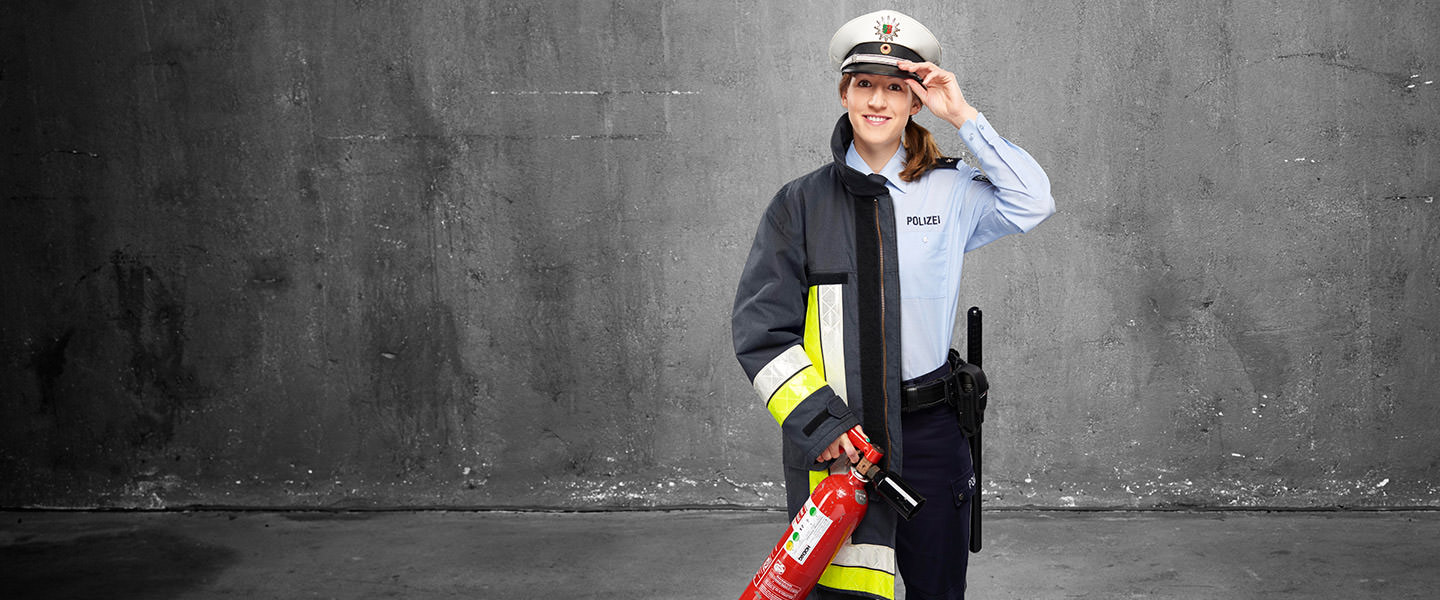 Fotomontage einer Frau: Halb Polizistin in Dienstkleidung, halb Feuerwehrfrau in Uniform. Mit einer Hand hält sie einen Feuerlöscher, mit der anderen greift sie an die Dienstmütze ihrer Polizeiuniform.