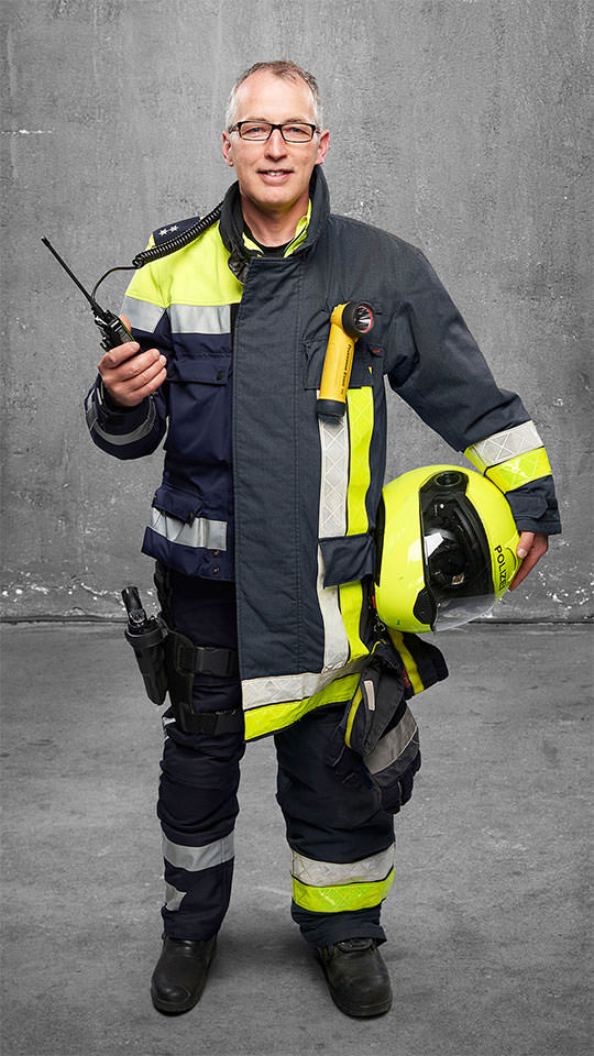 Fotomontage eines Mannes: Halb Motorradpolizist in Uniform, halb Feuerwehrmann in Uniform. Er hält ein Funkgerät in der Hand.