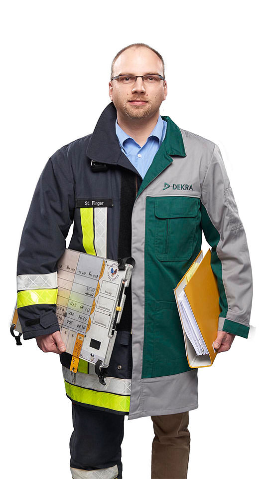 Fotomontage eines Mannes: Halb Prüfingenieur, halb Feuerwehrmann. In der linken Hand trägt er einen Aktenordner, in der rechten eine Atemschutzüberwachungstafel der Feuerwehr.